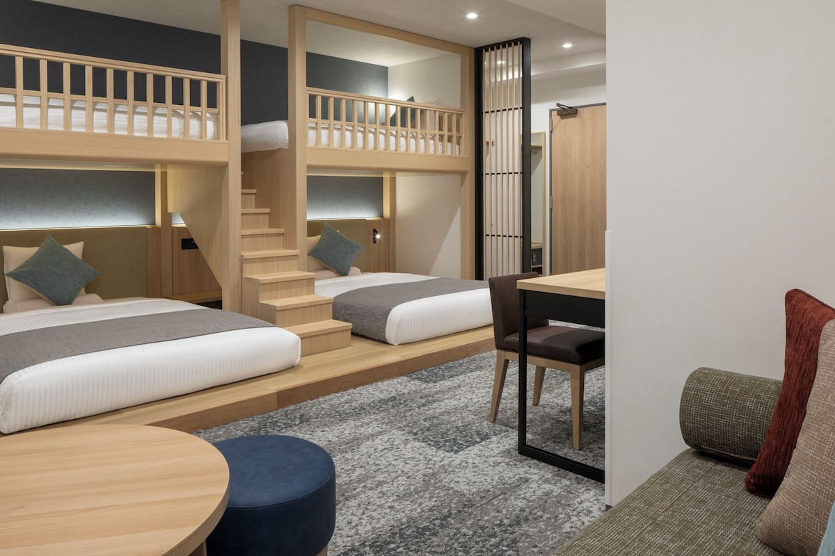 Quarto de hotel moderno com beliches, uma escrivaninha e um espaço de estar.