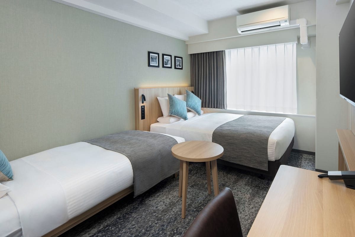 Quarto de hotel com duas camas de solteiro, uma pequena mesa redonda, televisão e ar condicionado.
