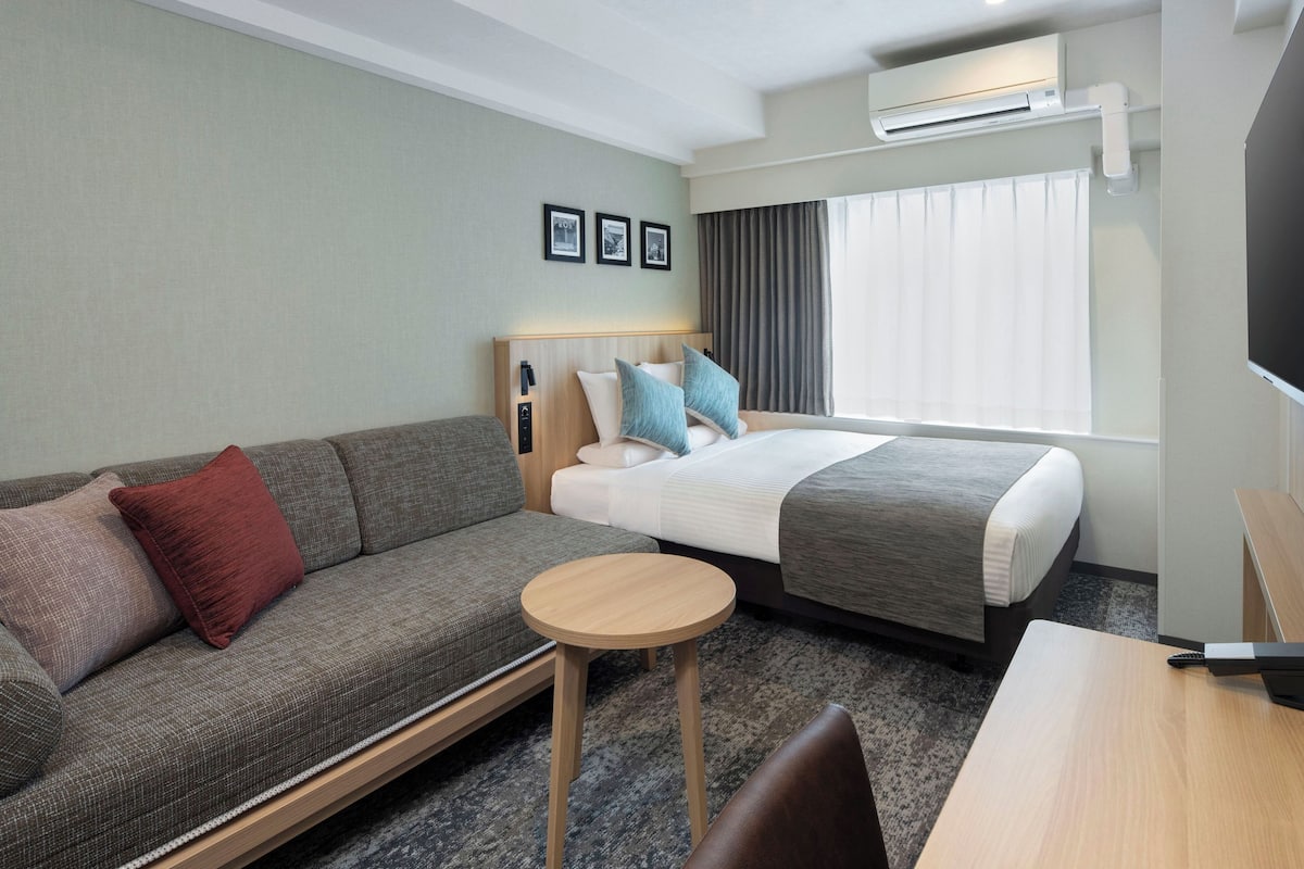 Quarto de hotel com uma cama, um sofá, uma mesa pequena e uma televisão.