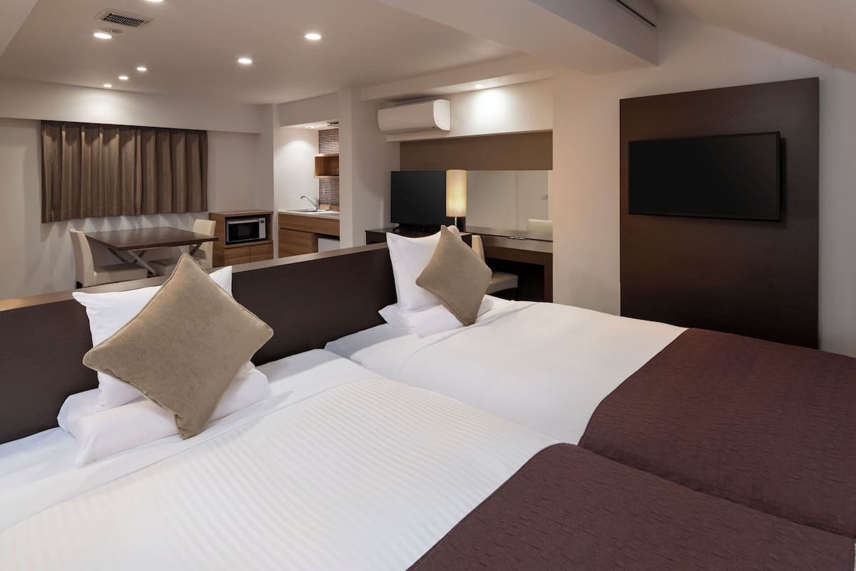 Quarto de hotel com duas camas, uma escrivaninha, televisão e banheiro.
