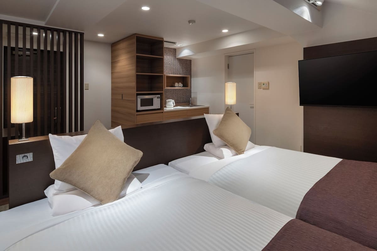 Quarto de hotel com duas camas, um minibar, uma televisão e parede revestida de madeira.