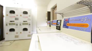 A laundromat with multiple washing machines and dryers, a sign for a 4.5 kg coin washer, and a metal rack for hanging clothes.