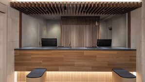 A reception desk with two computer monitors, wooden paneling, and a bench with a black seat. - HOTEL MYSTAYS Iidabashi (Tokyo)