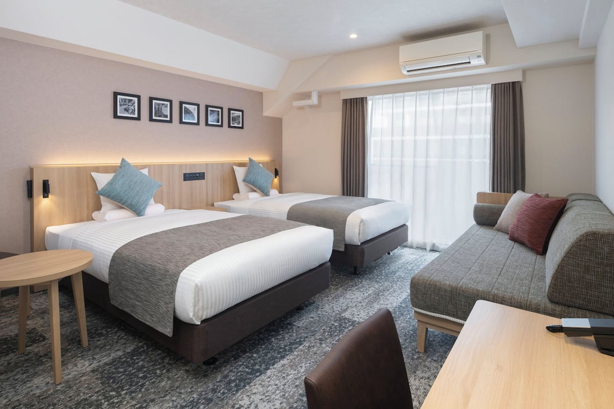 Quarto de hotel com duas camas, um sofá, uma mesinha e um ar condicionado.
