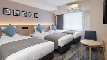 A hotel room with two beds, a small table, a chair, and a TV. There are framed pictures on the wall and an air conditioning unit above the window.