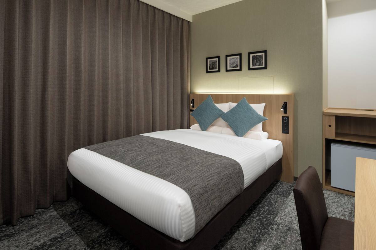 Quarto de hotel com uma cama grande, uma escrivaninha e uma cadeira. Há três quadros na parede acima da cama.