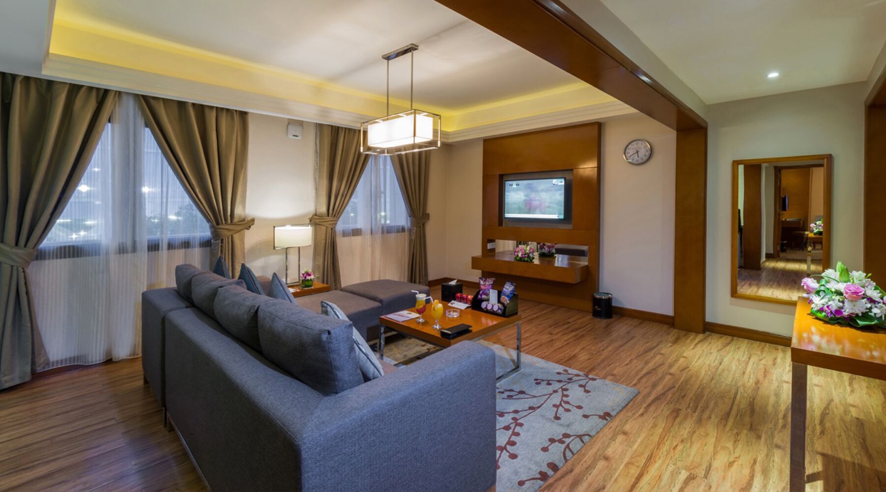 Een moderne hotelkamer met een bank, een salontafel, een televisie en een houten vloer.