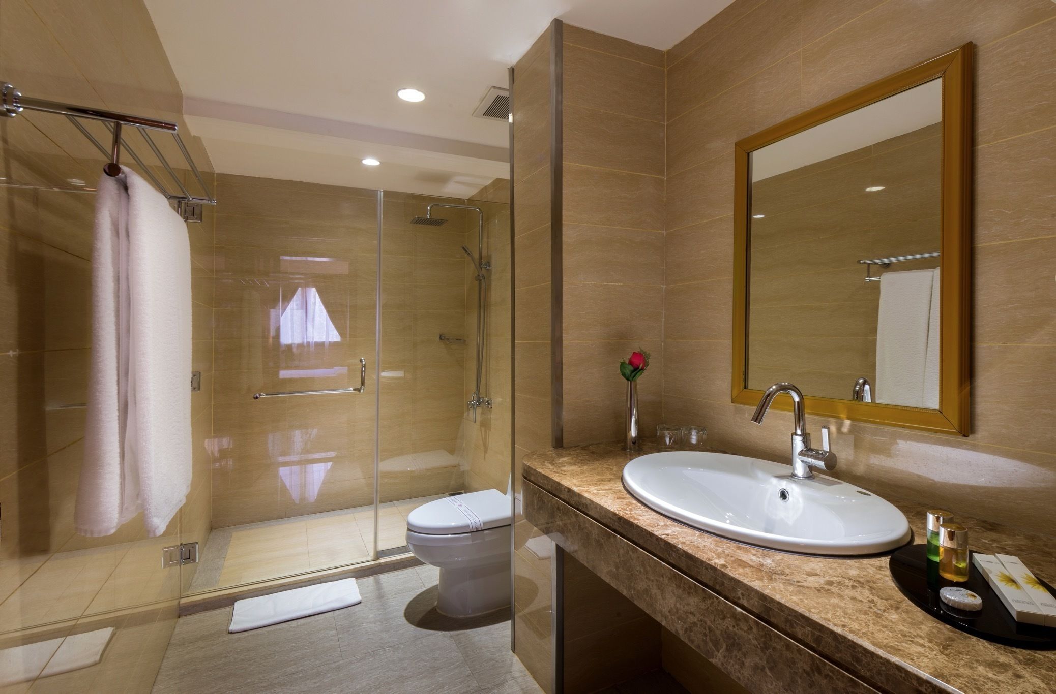 Ein modernes Badezimmer mit einer Duschkabine, einer Toilette, einem Waschbecken mit Spiegel und einer Rosenblume.