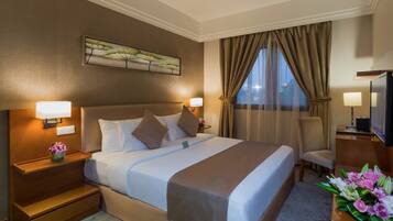 A hotel room with a large bed, two bedside lamps, a flat-screen TV, a desk with a lamp, and a window with curtains.