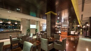 Un moderno vestíbulo de hotel con una zona de bar, espacios para sentarse y una escalera que sube a los pisos superiores.