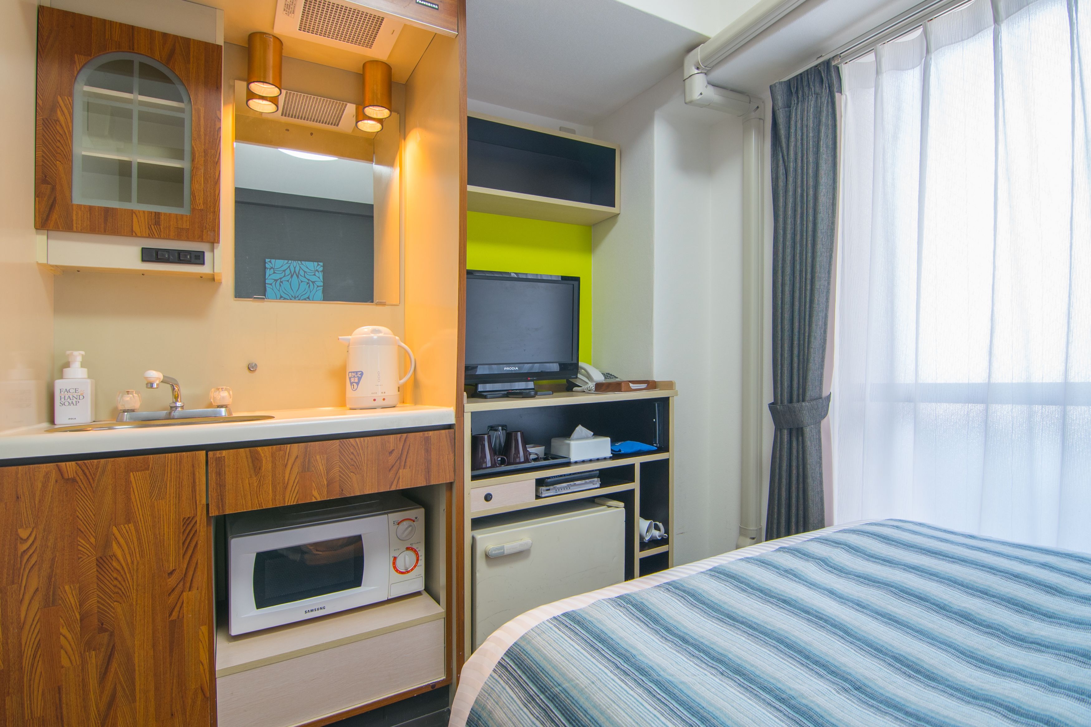 A hotel room with a bed, a microwave, a small refrigerator, a vanity with a mirror, and a television.