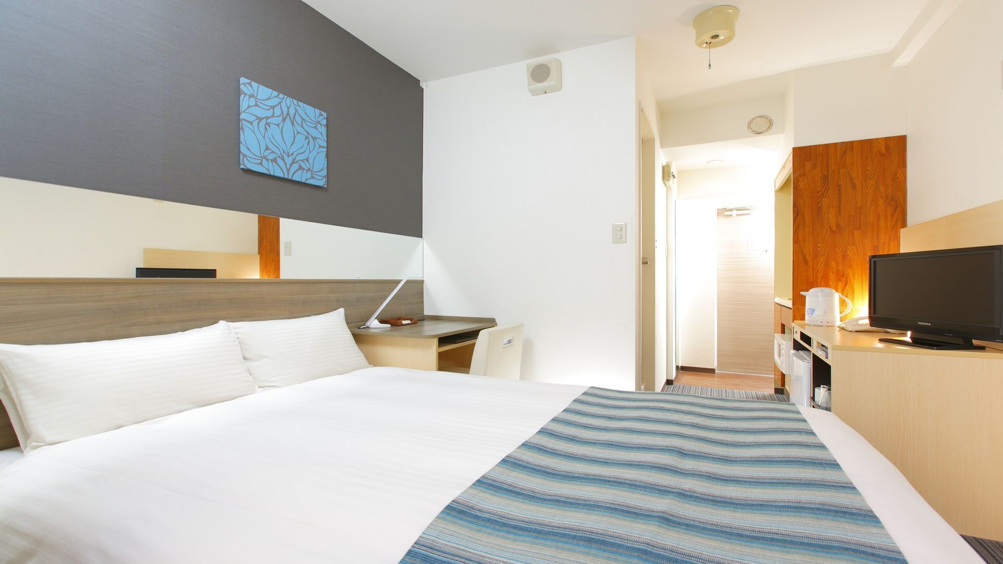 A hotel room with a bed, desk, TV, and a bathroom visible through an open door.