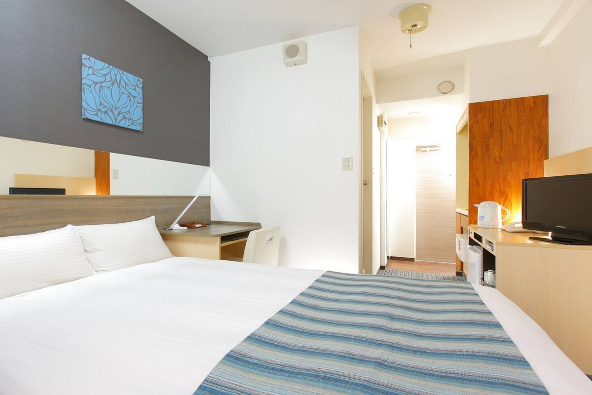 A hotel room with a bed, desk, TV, and a bathroom visible through an open door.