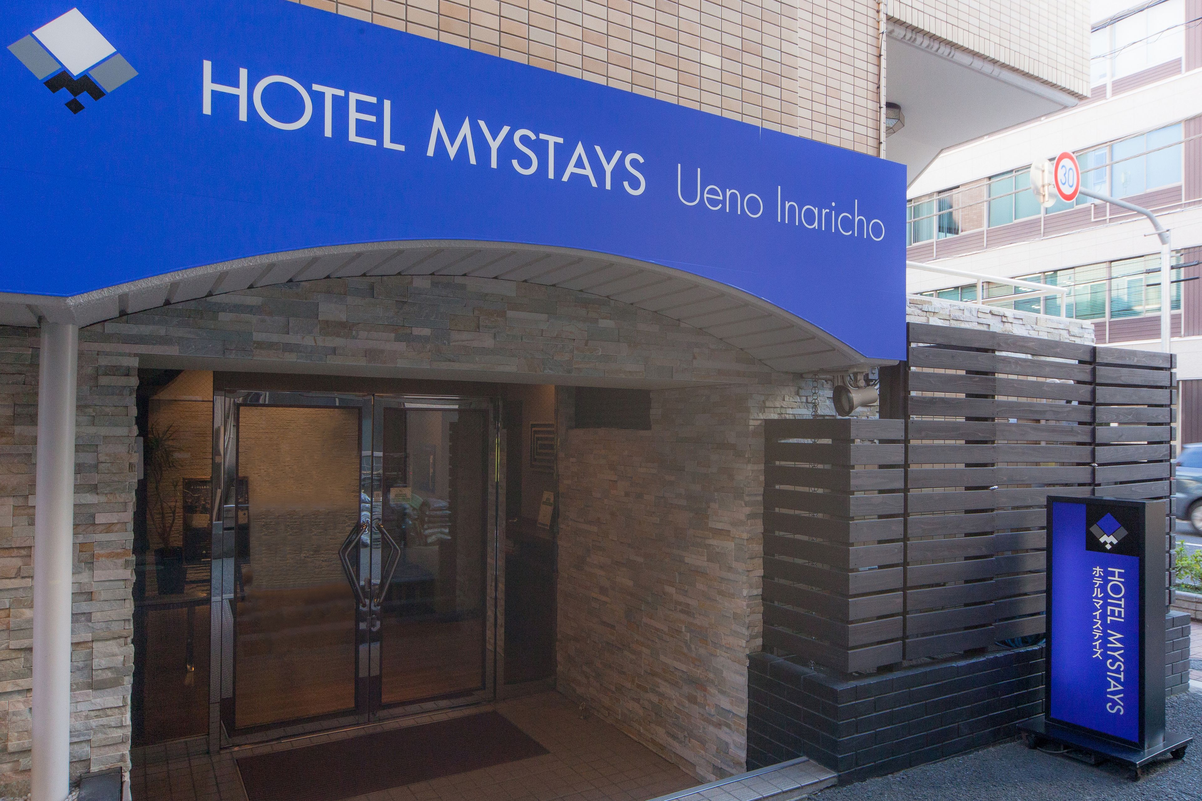 The entrance to Hotel Mystays with a clear sign above the door and a small signboard to the right.