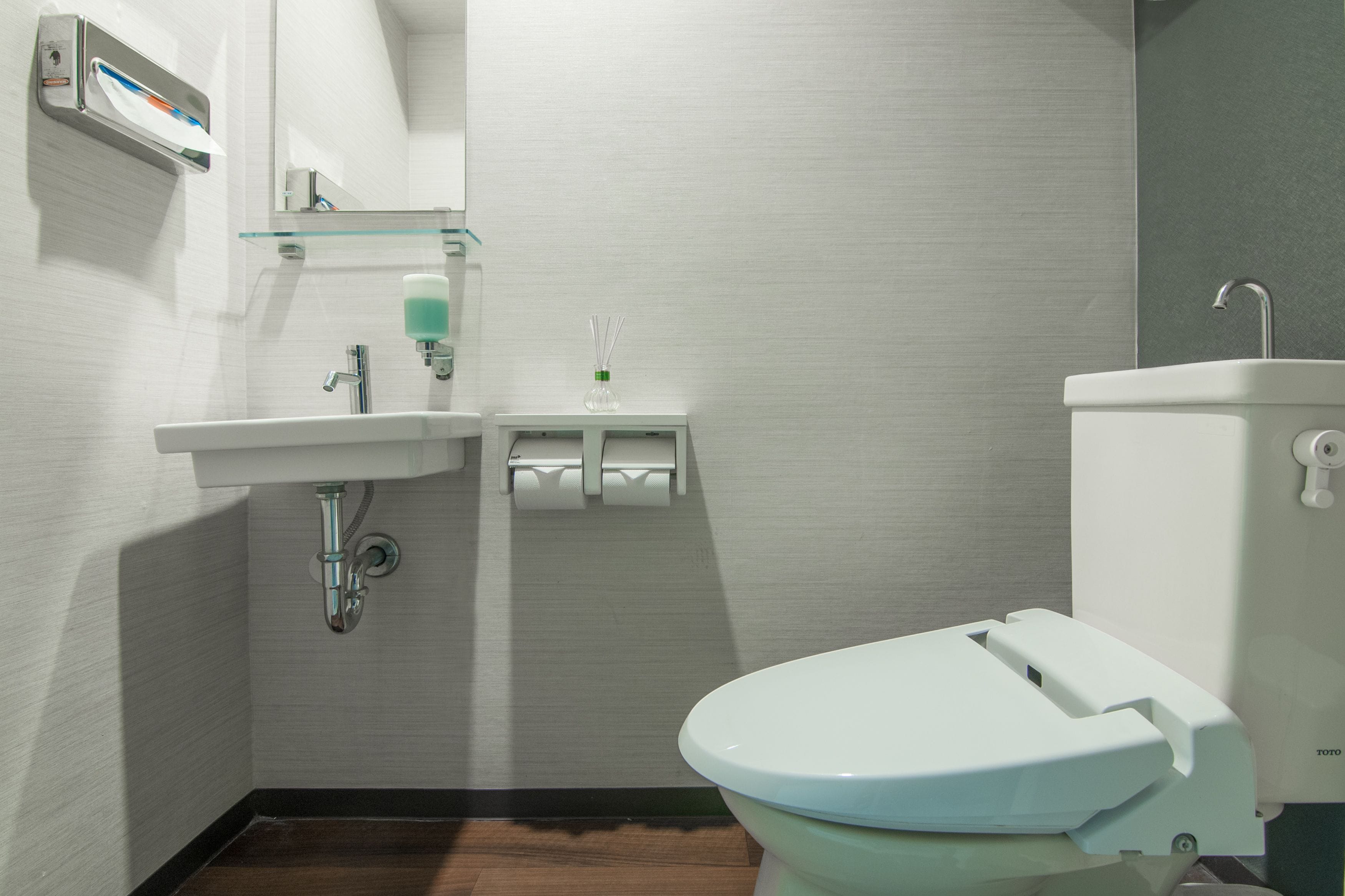 Une salle de bain moderne avec un lavabo blanc, des toilettes et une étagère en verre.