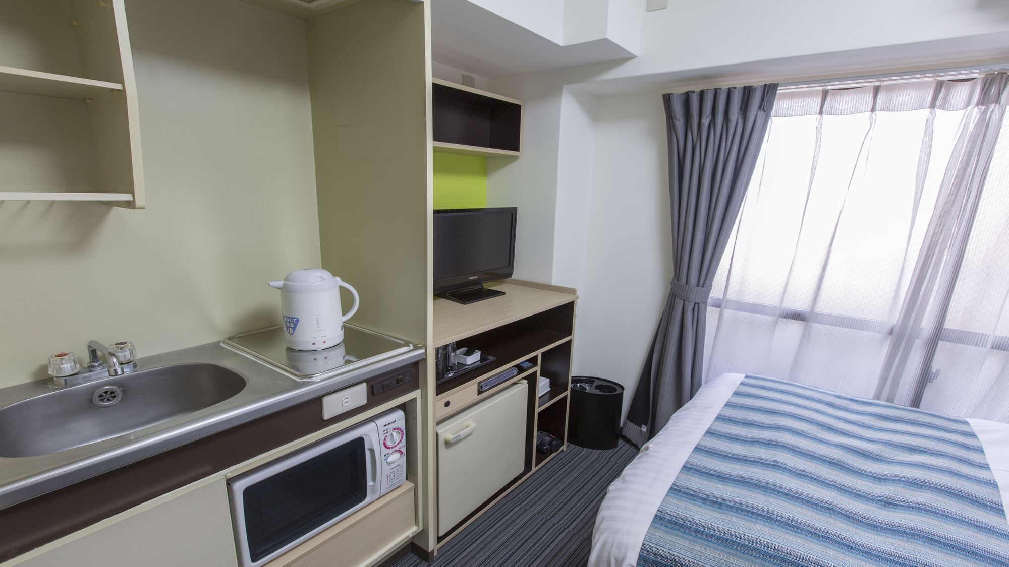 A hotel room with a bed, a TV, a coffee maker, a microwave, a sink, and a small cabinet.