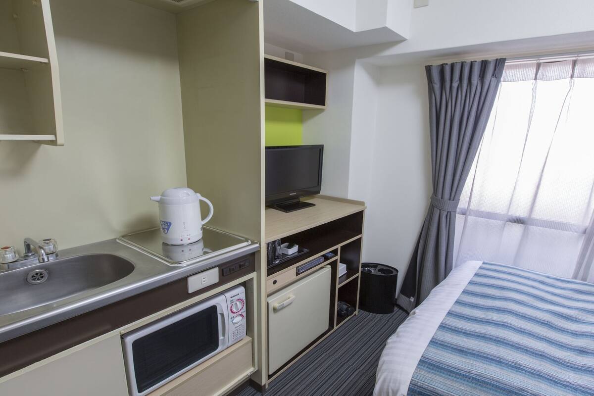 A hotel room with a bed, a TV, a coffee maker, a microwave, a sink, and a small cabinet.