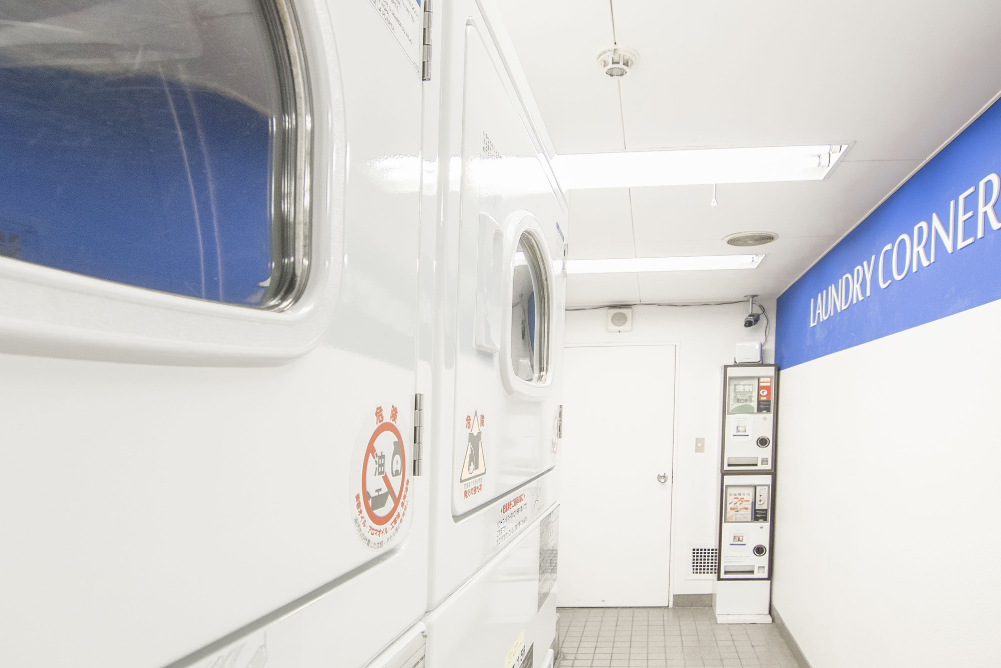 Une laverie avec une machine à laver blanche et un mur bleu sur lequel on peut lire le texte « LAUNDRY CORNER ».