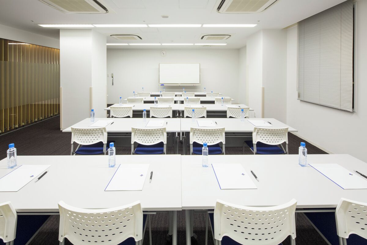 A conference room with white tables, perforated chairs, water bottles, and a whiteboard.