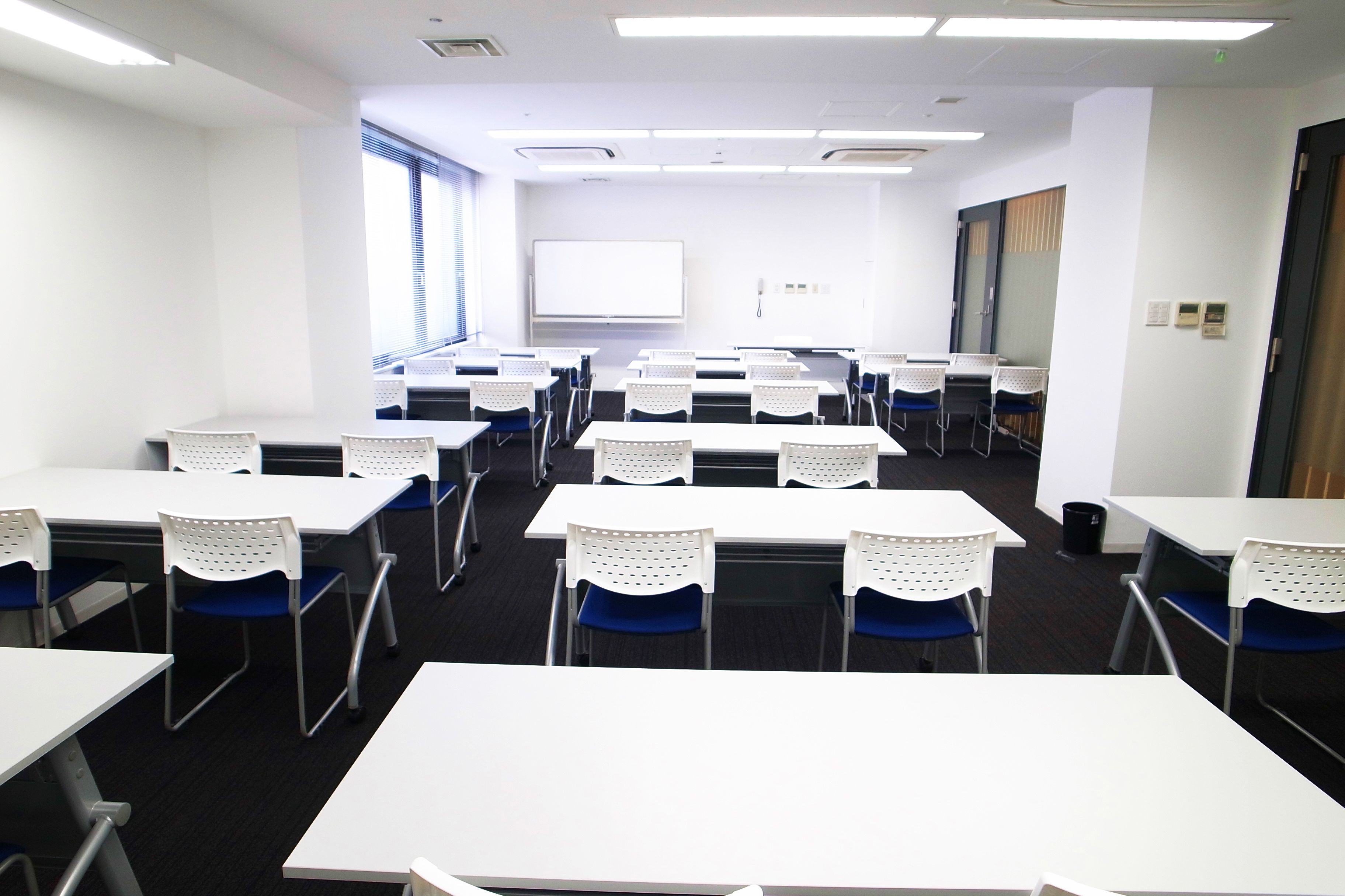 A conference room with white tables and chairs, a projector screen, and a whiteboard.