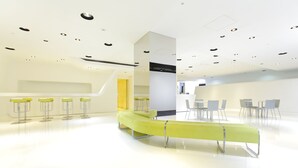 A modern interior with a central yellow bench, white walls, and a ceiling with recessed lighting. - Hotel MyStays Ochanomizu Conference Center (Tokyo)