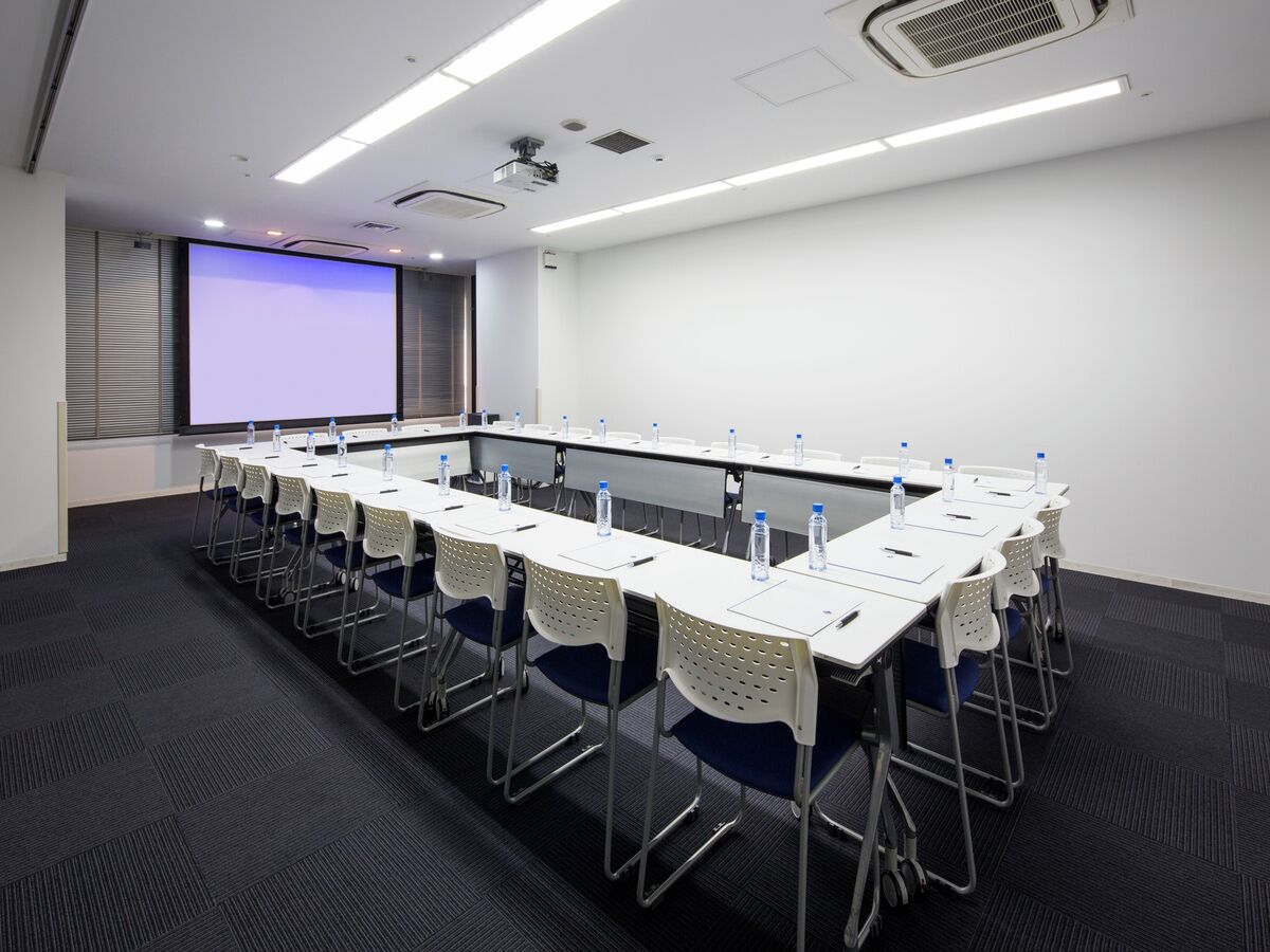 A conference room with a long table, chairs, water bottles, and a projector screen.