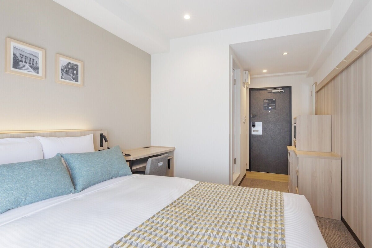 A hotel room with a bed, bedside table, lamp, and a door leading to another room.