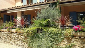 A building with a stone wall, potted plants, and a balcony with blue shutters.