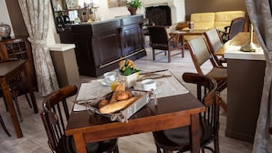 A dining area with a wooden table set for two, a kitchen area with a bar, and a living room with a sofa and chairs.