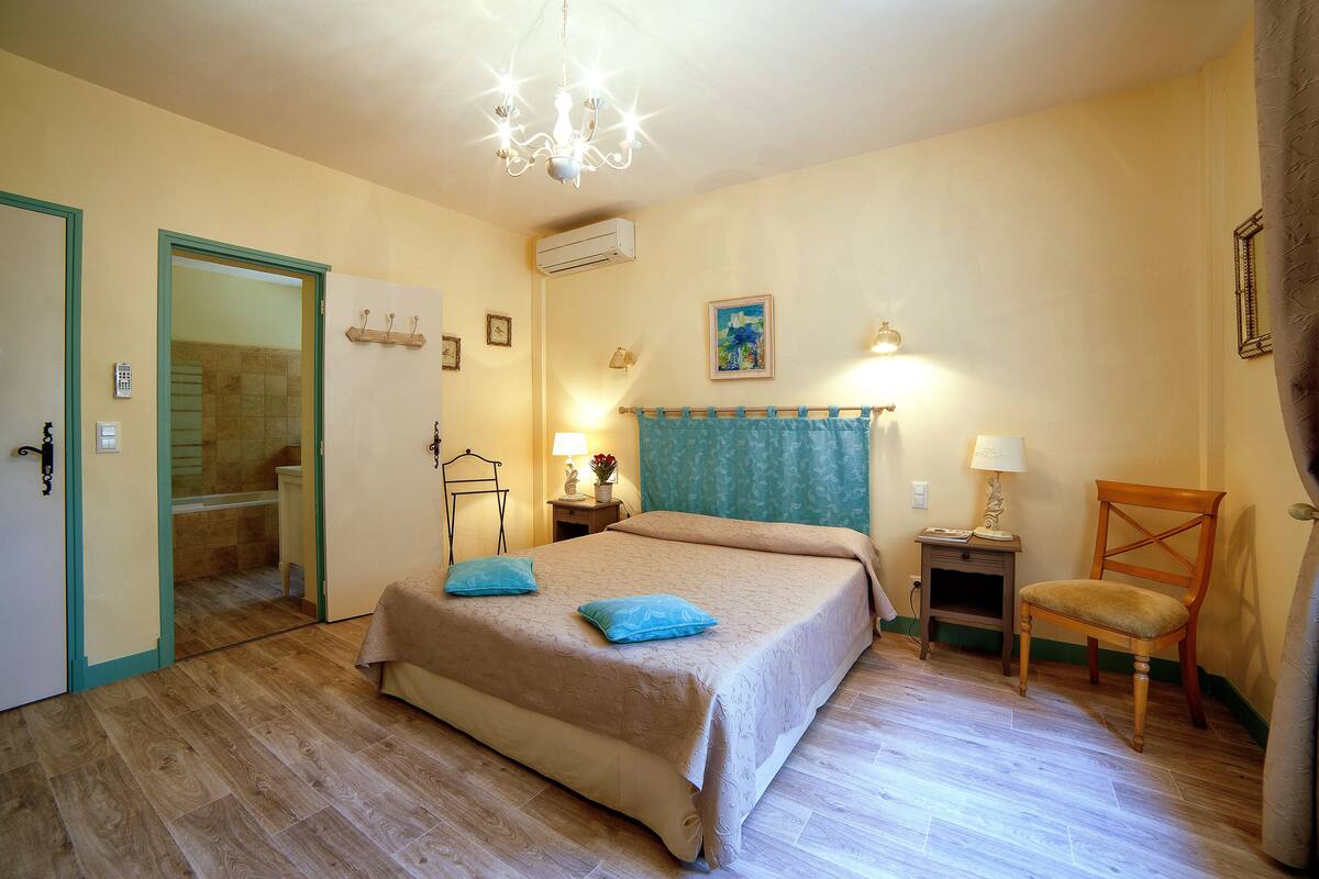 Une chambre à coucher comprenant un lit, une chaise, une table de chevet, une lampe et une porte donnant sur une salle de bain.