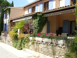 A two-story building with a stone facade, blue shutters, and a balcony with outdoor seating. - Hôtel Mistral (Mas-Blanc-des-Alpilles)