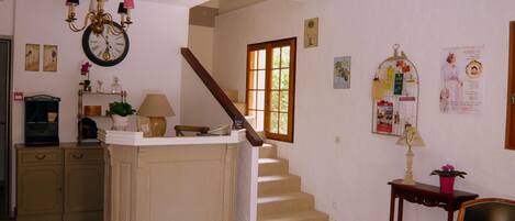 Un vaste espace de vie comprenant un escalier, un lustre, une horloge et un coin repas avec une table et des chaises.