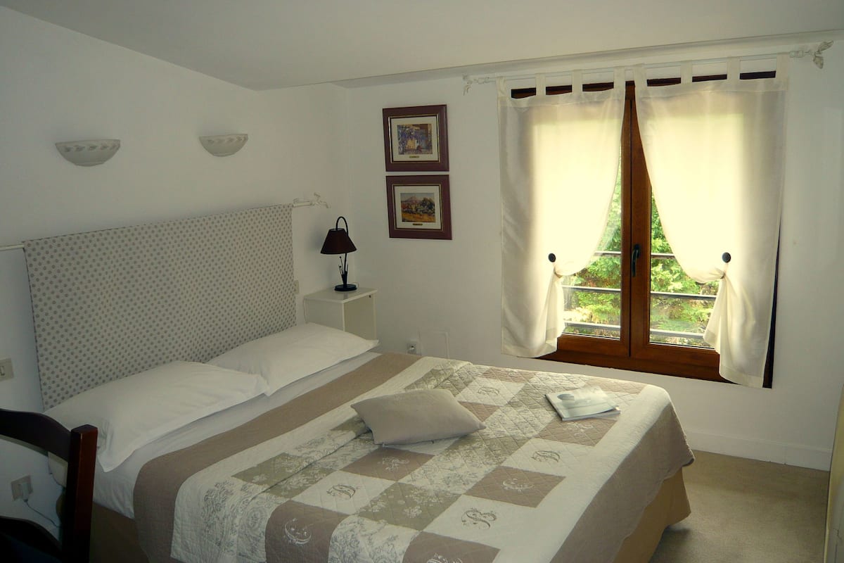 Un lit bien fait, avec une courtepointe, une lampe de chevet et deux tableaux encadrés accrochés au mur.