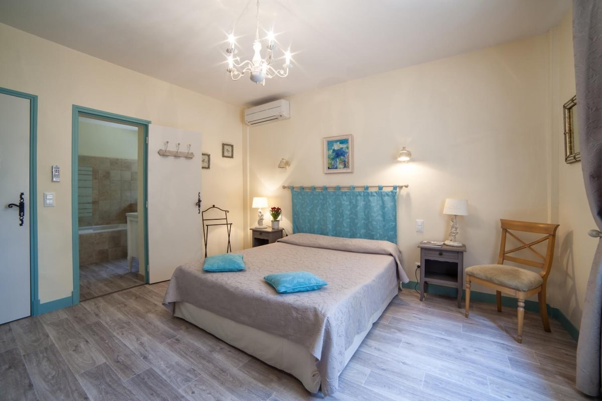 A bedroom with a bed, bedside tables, a chair, a chandelier, and a painting on the wall.