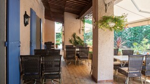 An outdoor patio area with wicker furniture, blue shutters, and potted plants.