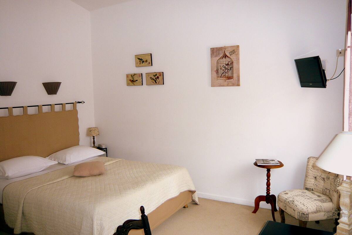 Une chambre à coucher comprenant un lit, une chaise, une petite table et des œuvres d’art accrochées au mur.