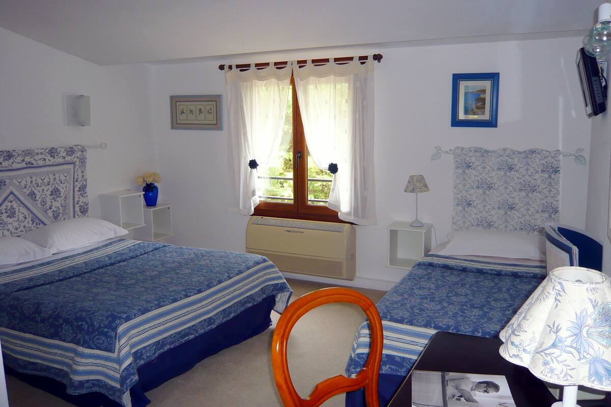 Une chambre avec deux lits, une fenêtre avec des rideaux, une table de chevet avec une lampe et une chaise.