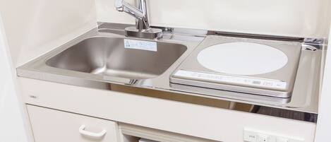 Una cocina compacta con un lavamanos de acero inoxidable, una estufa eléctrica empotrada y un lavavajillas blanco.