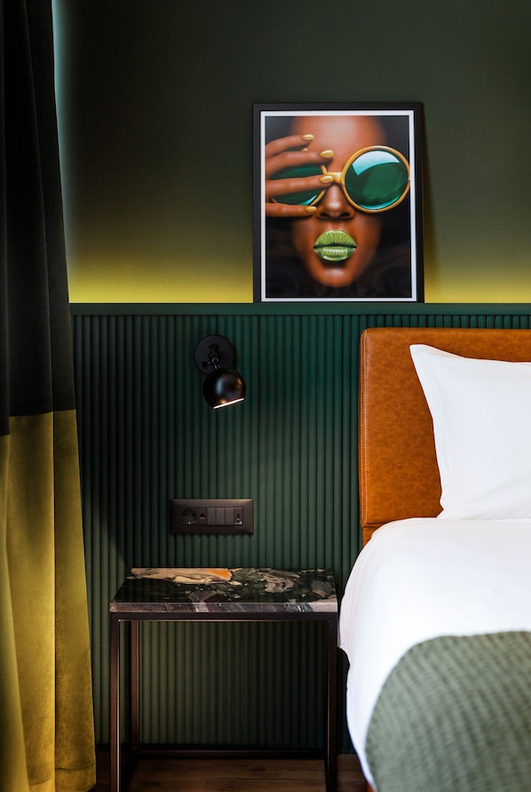 A hotel room with a bed, a nightstand, a wall-mounted lamp, and a framed picture.