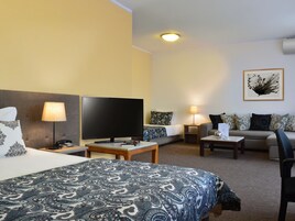Habitación de hotel con cama, televisión, sofá, mesa de centro y un cuadro en la pared.