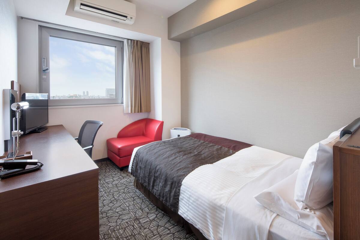 Ein Hotelzimmer mit Bett, Schreibtisch, Stuhl, Fernseher und einem fenster mit Vorhängen.