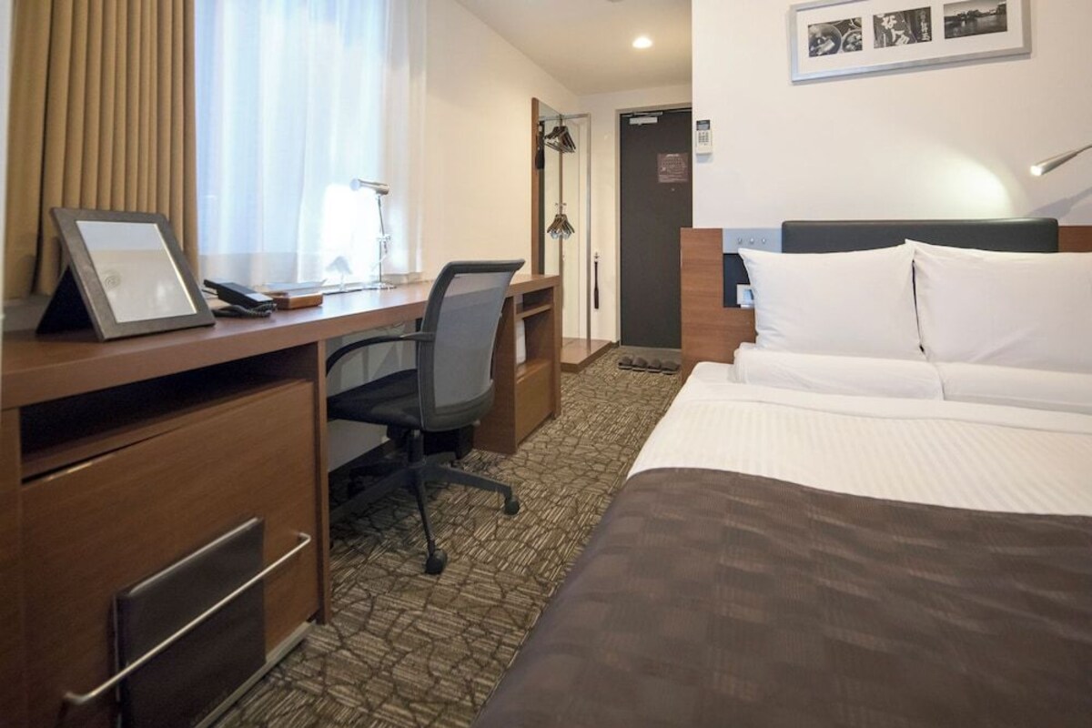 Une chambre d’hôtel équipée d’un lit, d’un bureau, d’une chaise et d’une porte donnant sur un espace douche.