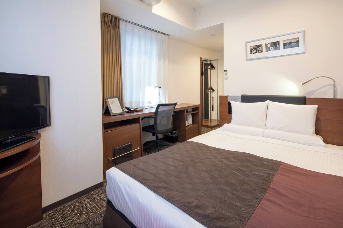 Ein Hotelzimmer mit Bett, Schreibtisch, Stuhl, Fernseher und Spiegel.