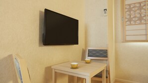 Ein kleiner Raum mit an der Wand montiertem Fernseher, einem Tisch mit zwei Schüsseln, einem Stuhl und Holzboden.