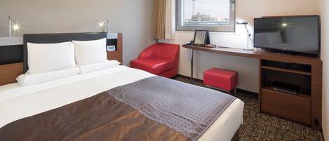 Une chambre d’hôtel avec un lit, une chaise rouge, un bureau avec une télévision et une fenêtre donnant sur la ville.