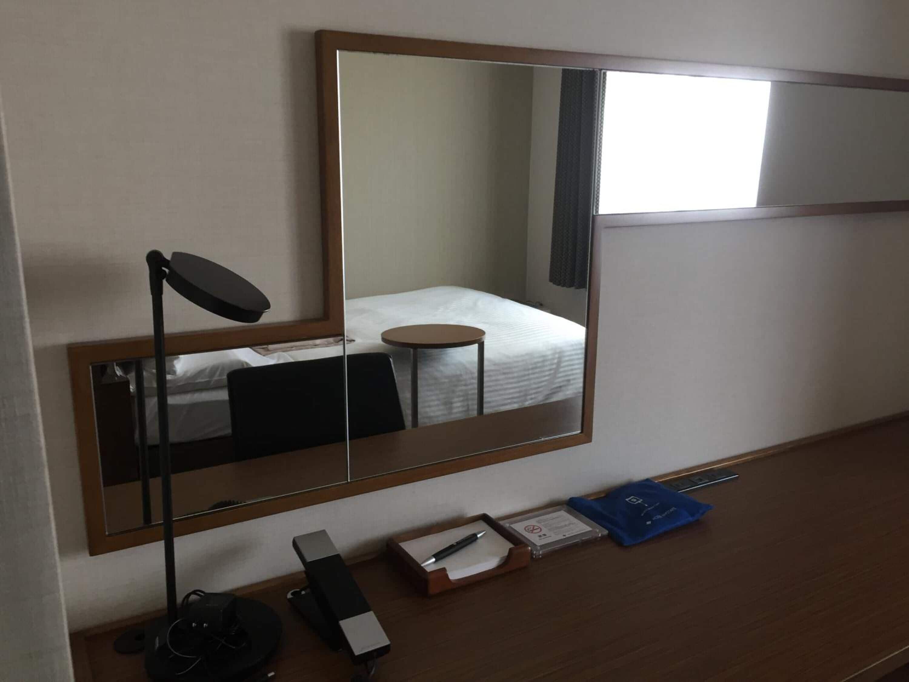 Habitación de hotel con un espejo grande, un escritorio con lámpara, una cama y una mesita.