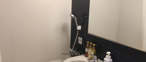 A bathroom with a white sink, a mirror, a handheld showerhead, and toiletries on the counter.