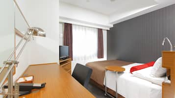A hotel room with a wooden desk, a bed with white and red bedding, a TV, a desk lamp, and a window with curtains.