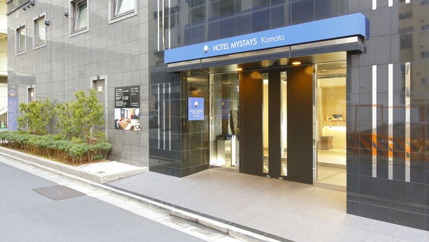 A modern hotel entrance with a blue sign, glass doors, and a tiled facade. - Hotel MyStays Kamata (Tokyo)