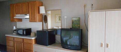 A hotel room with wooden cabinets, a microwave, a television, a bed, and a wardrobe.